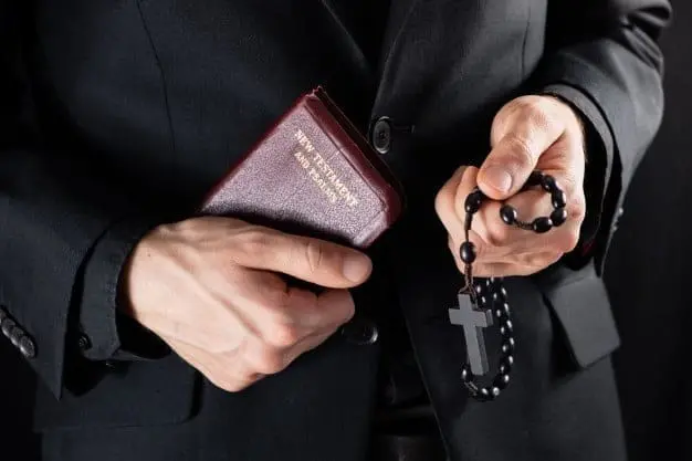 handen van een christelijke priester in het zwart gekleed met een kruisbeeld en een nieuwtestamentisch boek religieuze persoon met bijbel en gebedskralen ingehouden afbeelding 145134 240